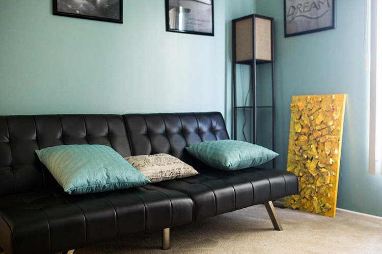A black futon sits in front of a teal wall