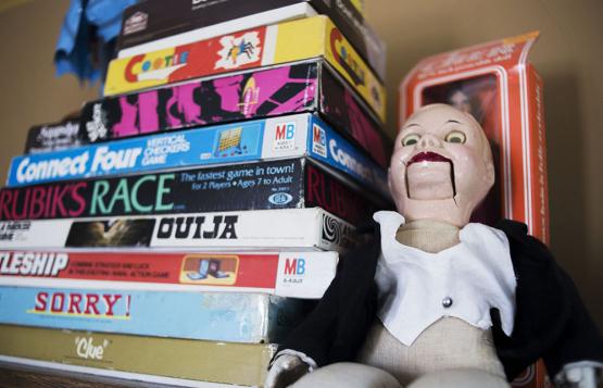 A ventriloquist dummy sits next to a stack of board games.
